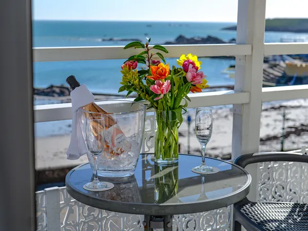 Ice bucket with a bottle of rosé, two flutes and a vase of colourful flowers on a balcony overlooking the sea.