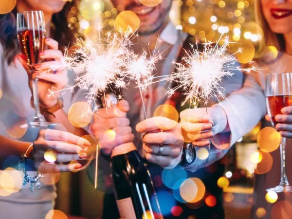 Friends celebrating at a festive party with sparklers, champagne flutes and a bottle of sparkling wine