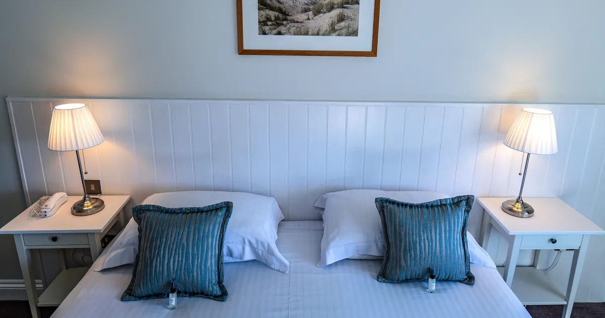 Twin bedroom at Ommaroo Hotel with white bedside tables, matching lamps and blue accent cushions