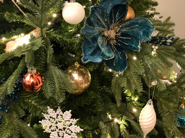 Close-up of a decorated Christmas tree with teal, gold and white baubles, warm fairy lights and a large teal floral ornament.