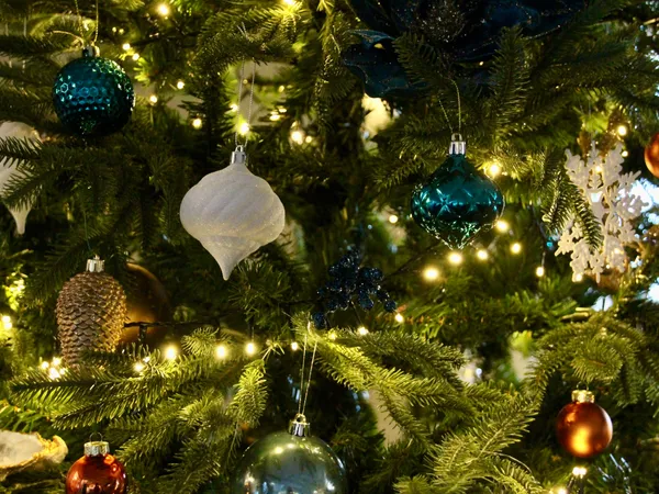 Close-up of a decorated Christmas tree with blue, white and copper baubles, a white snowflake ornament and warm fairy lights.