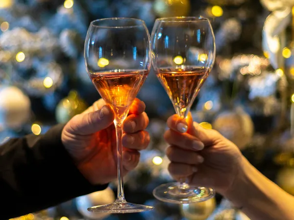 Two people clinking glasses of rosé wine in front of a softly lit Christmas tree.