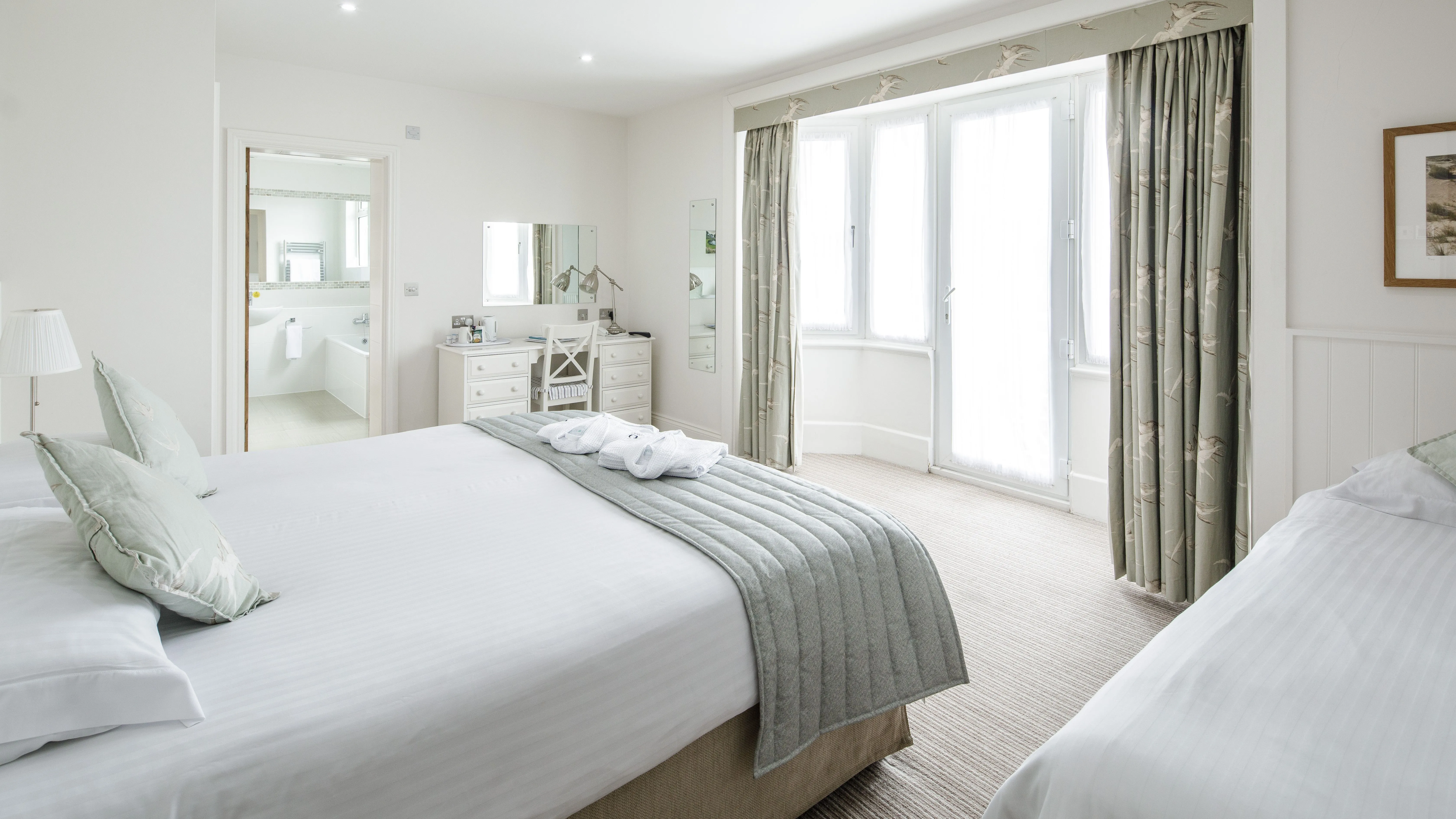 Bright triple room with a double bed, single bed, dressing table, en-suite bathroom and large bay window with patterned curtains.