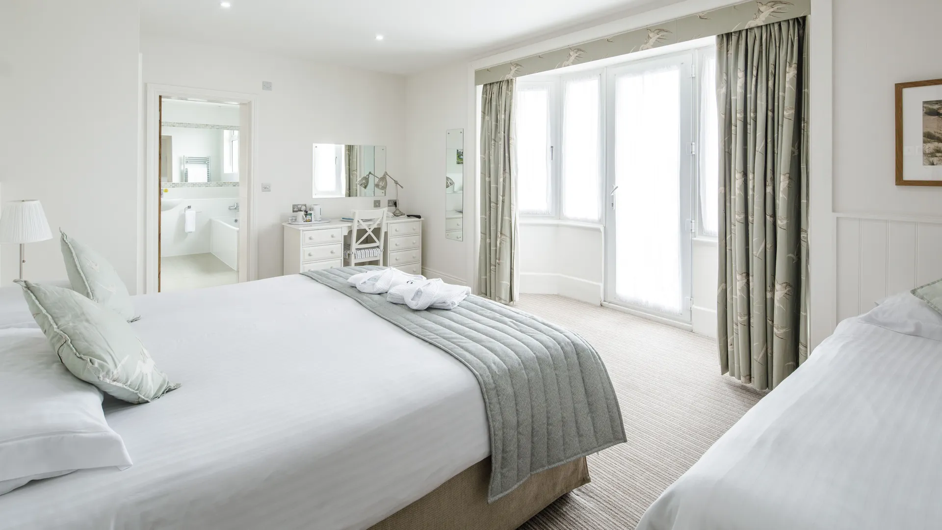 Bright triple room with a double bed, single bed, dressing table, en-suite bathroom and large bay window with patterned curtains.