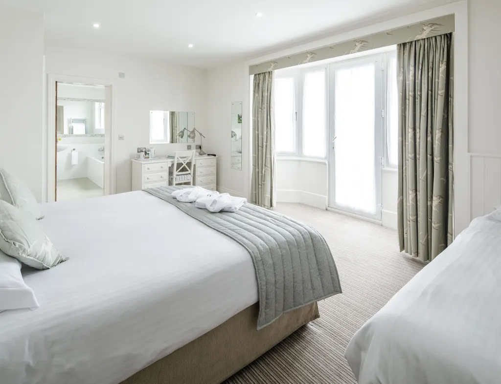 Bright triple room with a double bed, single bed, dressing table, en-suite bathroom and large bay window with patterned curtains.