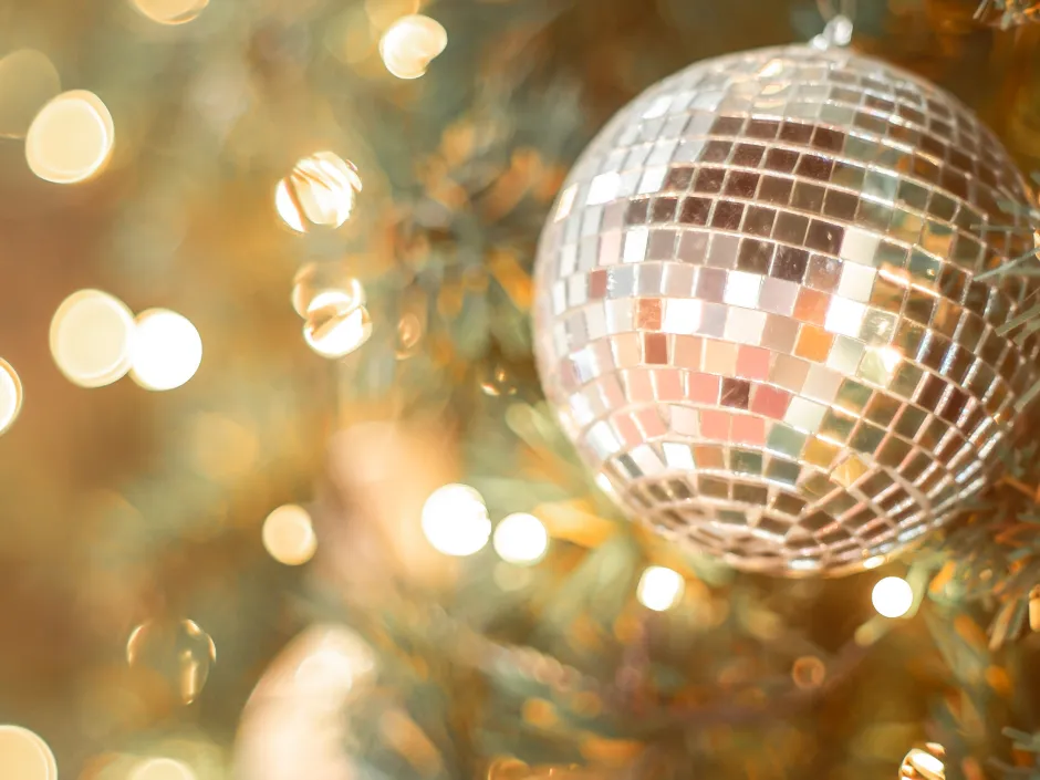 Silver mirrored bauble hanging on a Christmas tree with warm glowing lights in the background