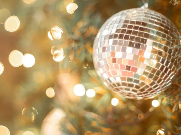 Silver mirrored bauble hanging on a Christmas tree with warm glowing lights in the background