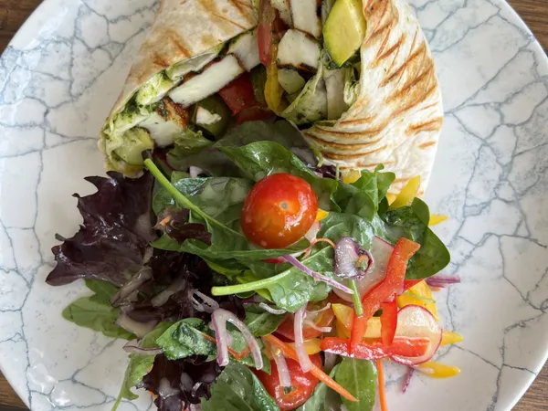 Grilled halloumi wrap filled with salad vegetables, served with a mixed leaf side salad on a marbled plate.