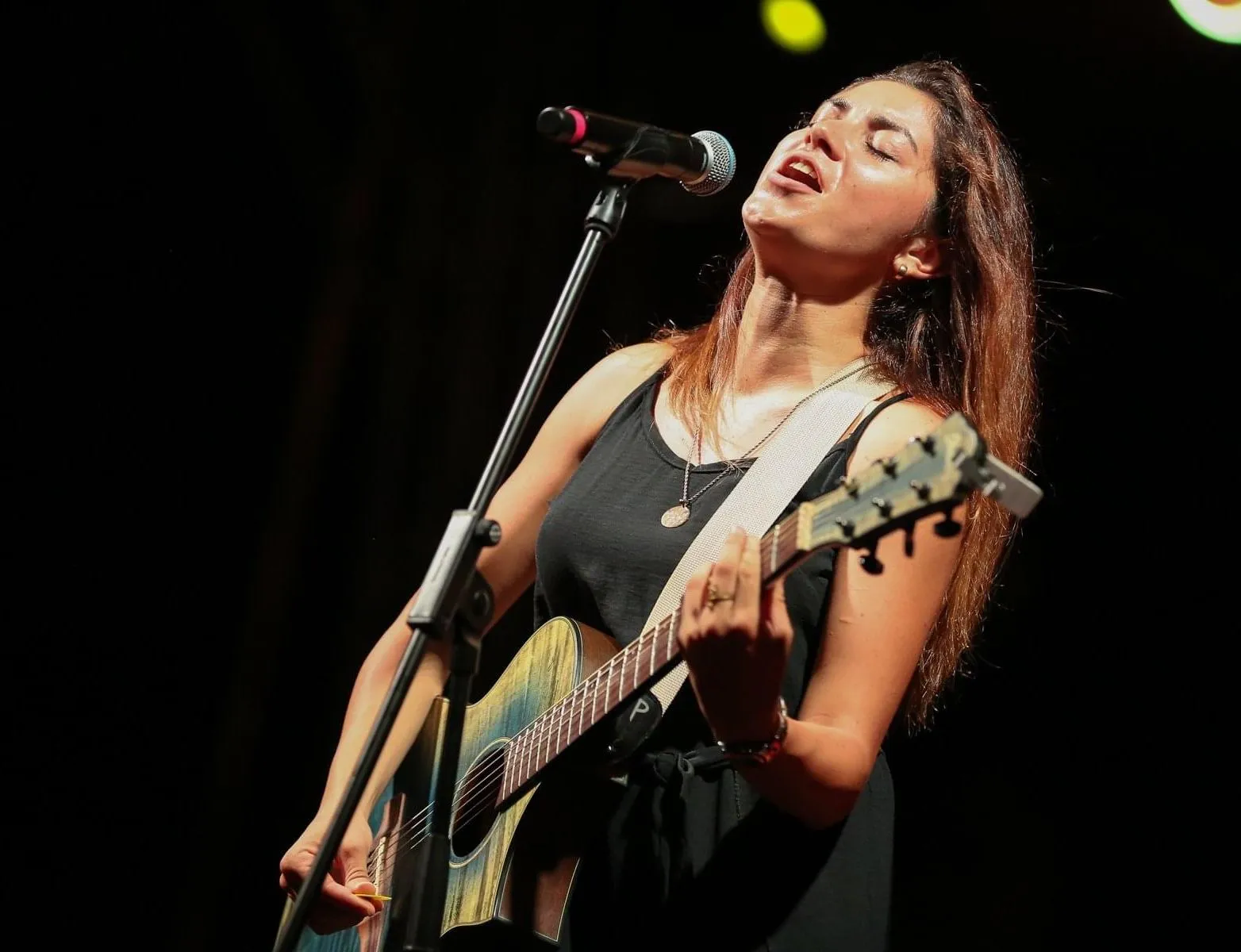 Cheryl Balzan performing on stage with an acoustic guitar and microphone