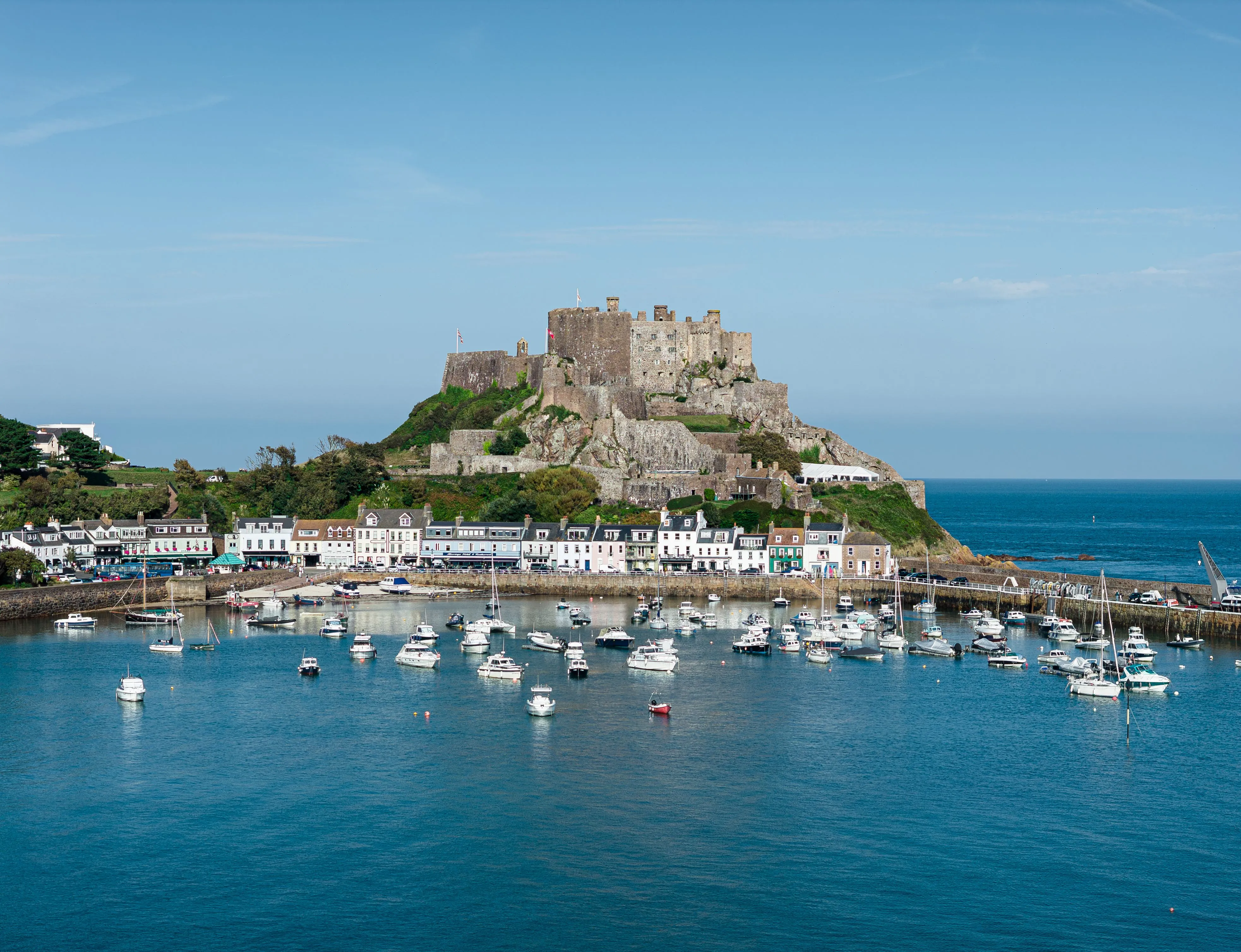 Mont Orgueil Castle overlooking Gorey Harbour, Jersey, with fishing boats moored in calm blue water.