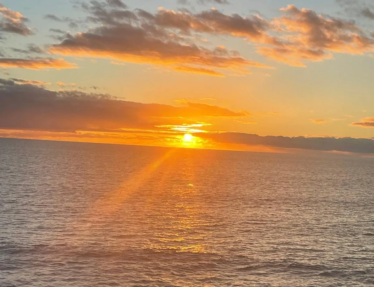 Golden sunset over a calm sea with glowing clouds and a rocky shoreline