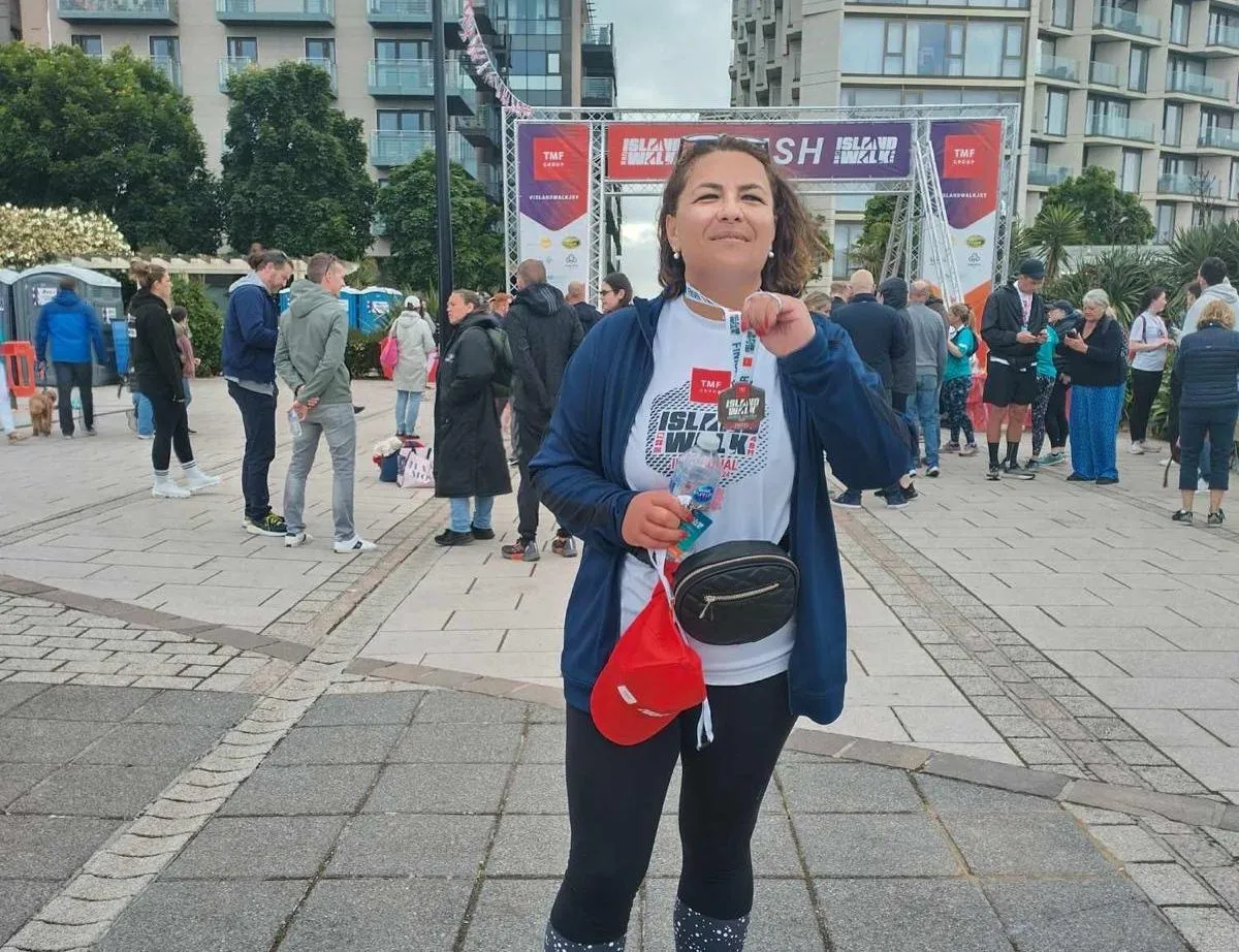 Woman wearing a finisher's medal at the Island Wolf Run event entrance, with crowds and modern flats behind her.