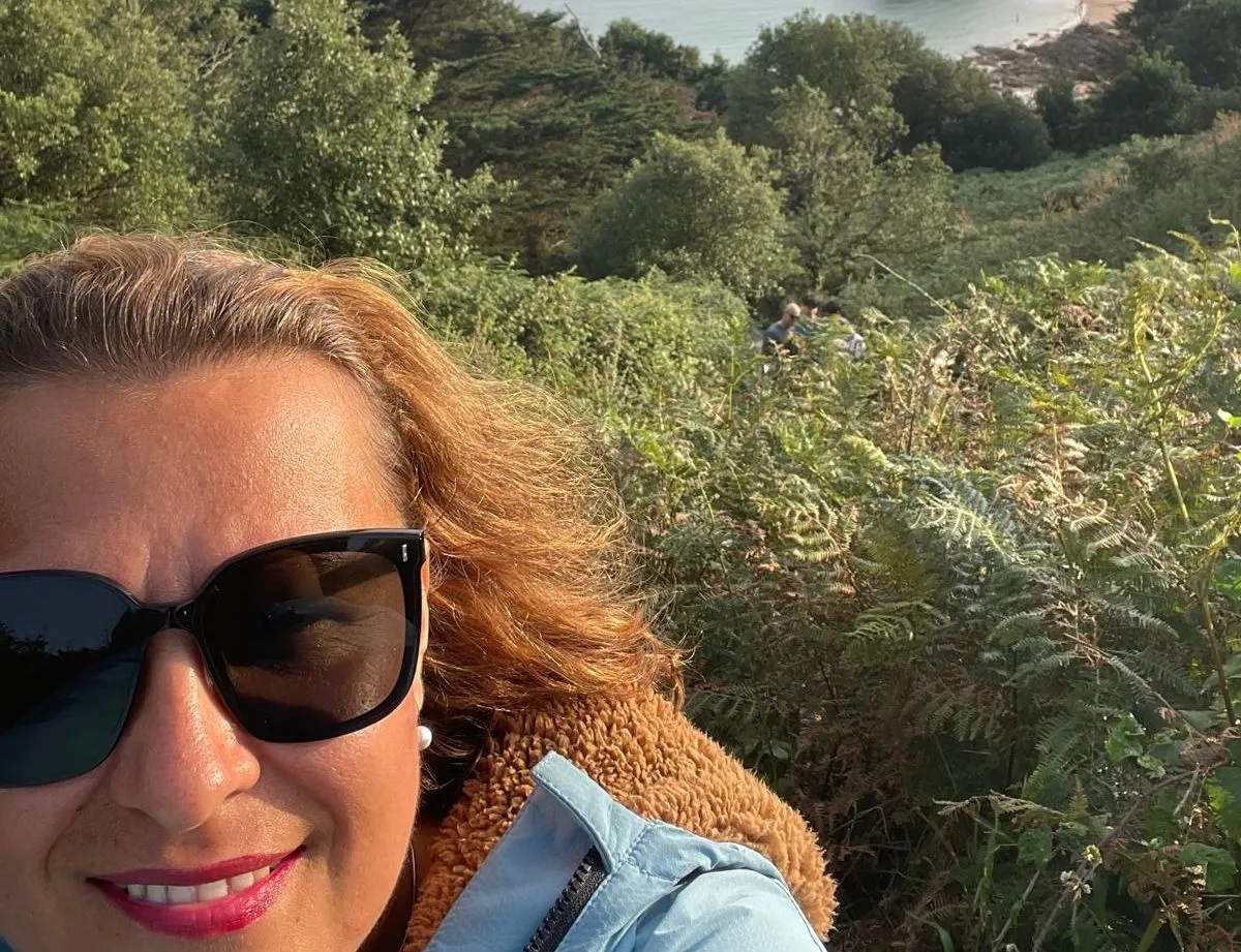 Woman in sunglasses taking a coastal selfie above a rocky islet and calm sea