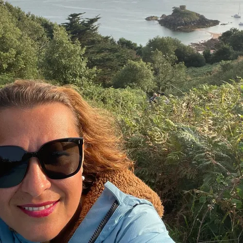 Woman in sunglasses taking a coastal selfie above a rocky islet and calm sea