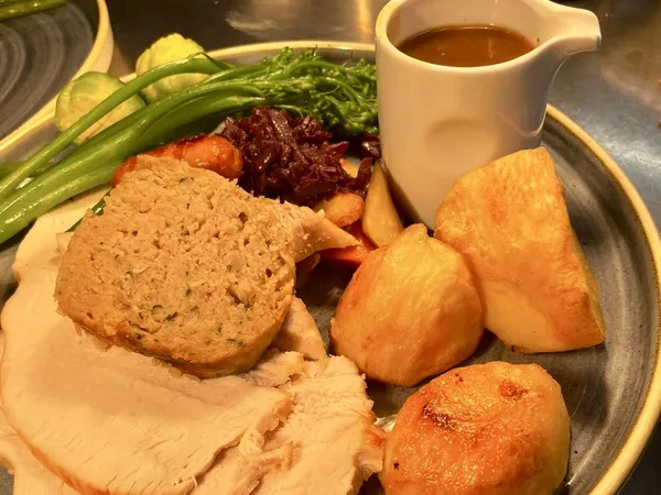 Roast turkey dinner with stuffing, roast potatoes, greens, red cabbage and gravy