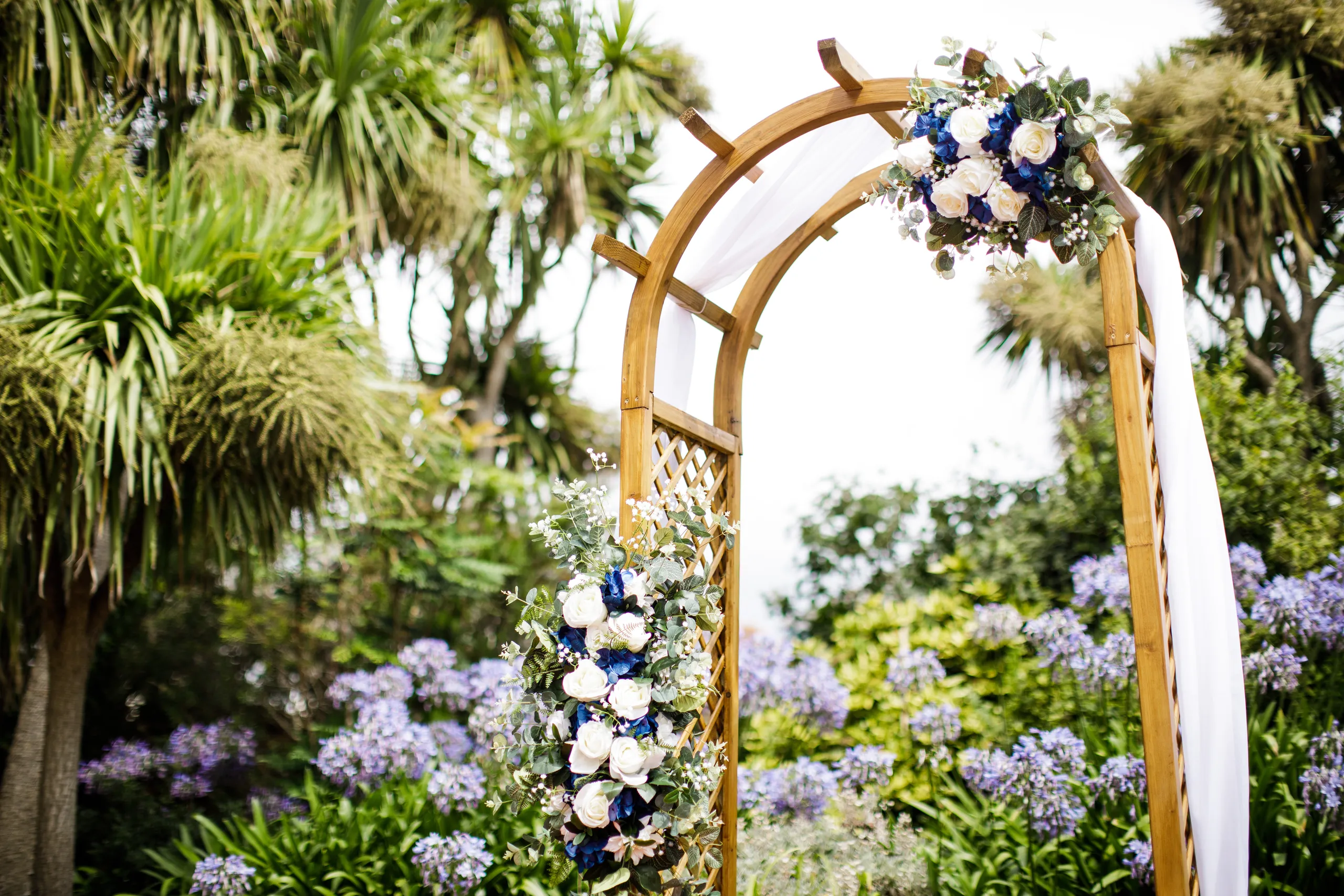 Wooden wedding arbour decorated with white and blue flowers in a lush garden setting