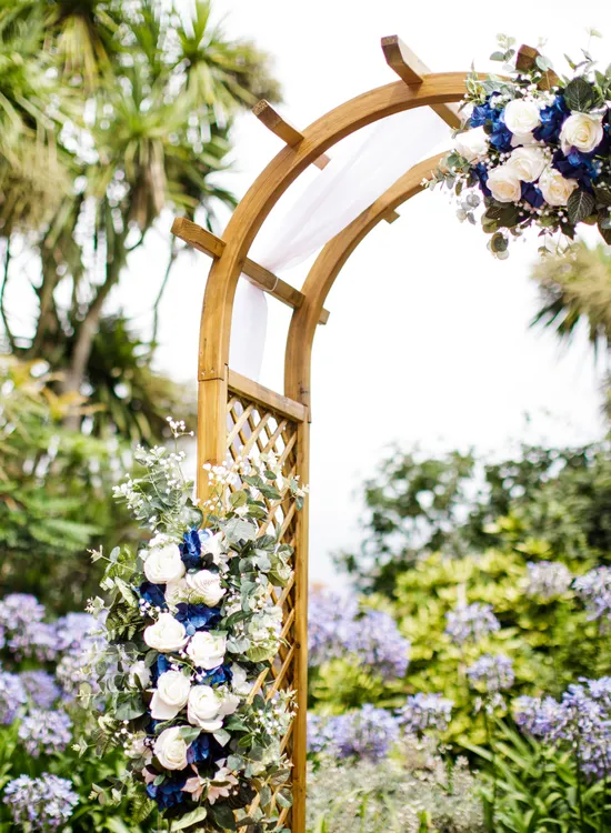 Wooden wedding arbour decorated with white and blue flowers in a lush garden setting