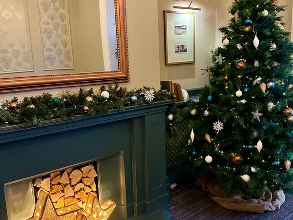Decorated Christmas tree beside a teal fireplace with glowing star lights and festive garland.
