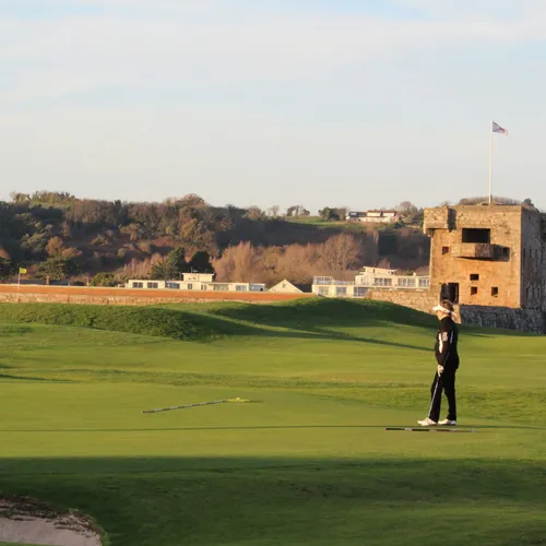 Two golfers on the green at Royal Jersey Golf Course beside a historic stone tower.