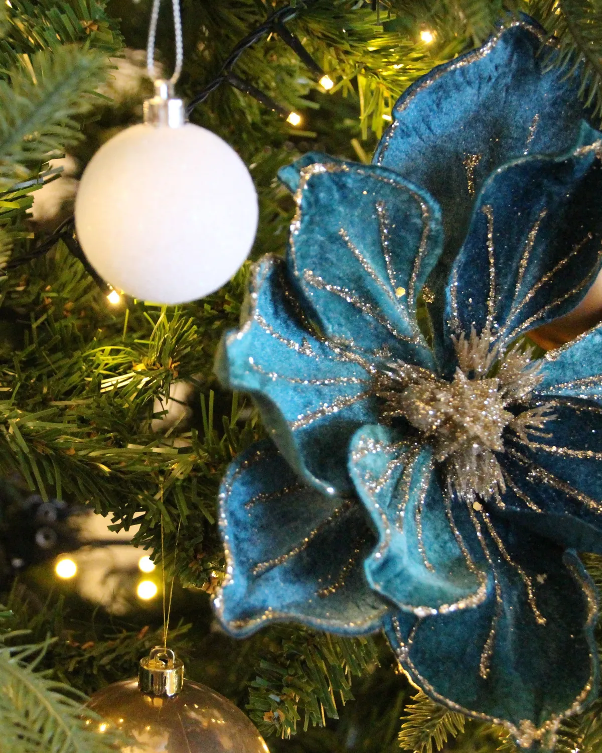 Close-up of a decorated Christmas tree with teal velvet poinsettia, baubles and warm fairy lights