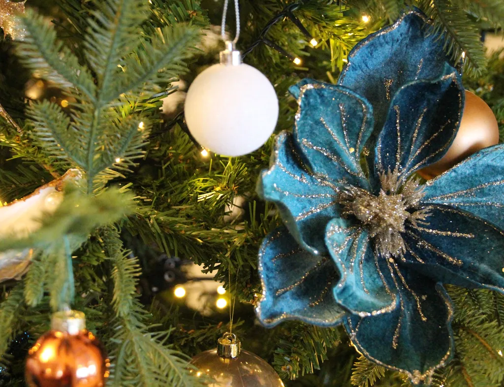 Close-up of a decorated Christmas tree with teal velvet poinsettia, baubles and warm fairy lights