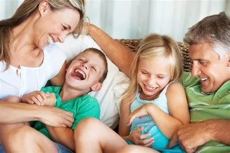 Smiling parents playfully tickling their laughing young son and daughter on a sofa.