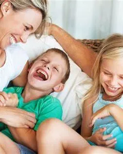 Smiling parents playfully tickling their laughing young son and daughter on a sofa.