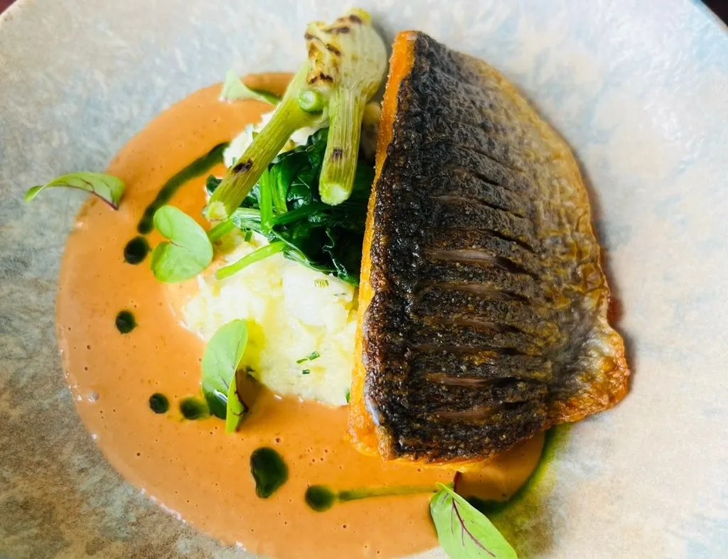 Crispy-skinned bream fillet with greens, purée and creamy orange sauce on a ceramic plate