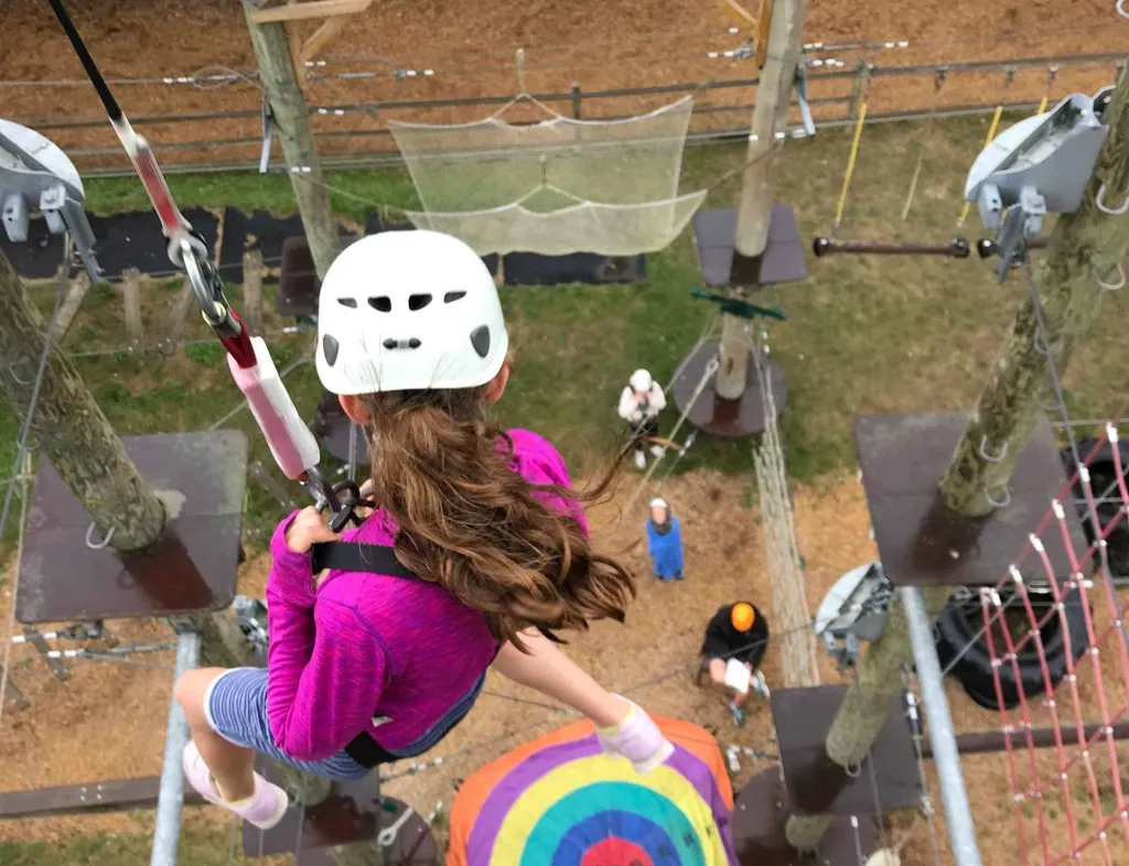 Helmeted child on a high ropes course above a colourful circular target