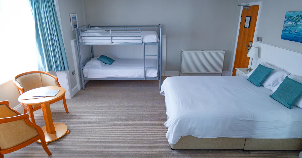 Spacious family hotel room with a double bed, bunk beds, seating area and blue curtains