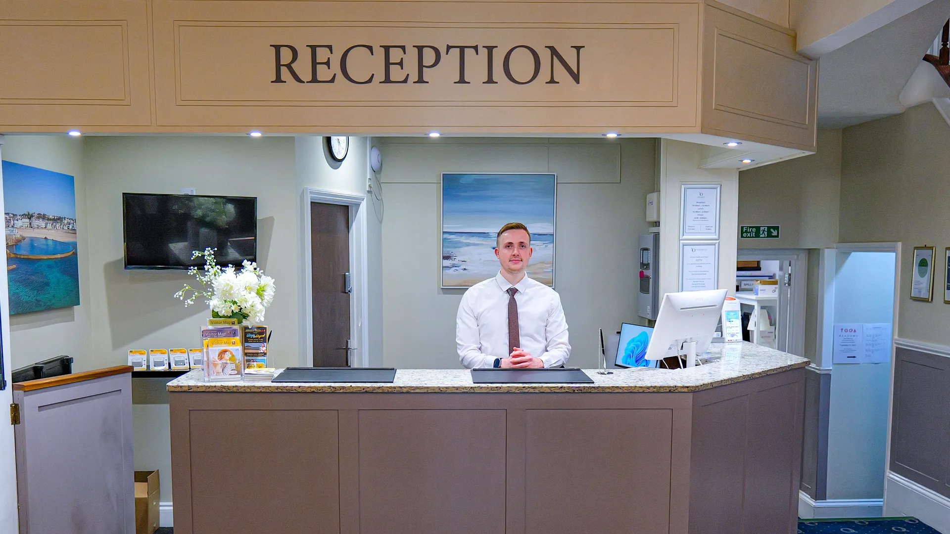 Hotel reception desk with a receptionist standing behind the counter in a bright, welcoming lobby