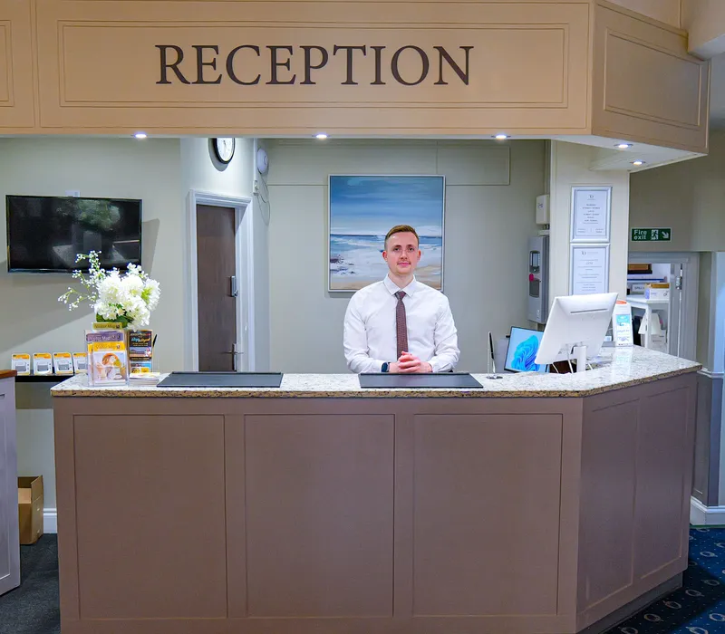 Hotel reception desk with a receptionist standing behind the counter in a bright, welcoming lobby