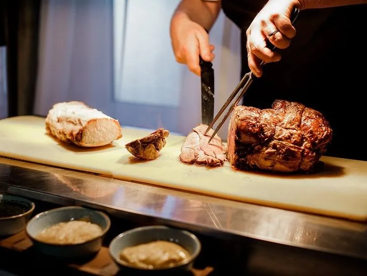 Chef carving roasted meat on a chopping board in a kitchen