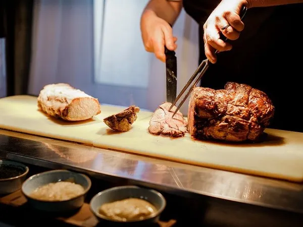 Chef carving roasted meat on a chopping board in a kitchen