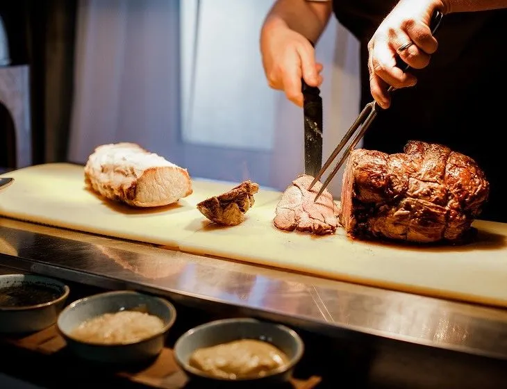 Chef carving roasted meat on a chopping board in a kitchen