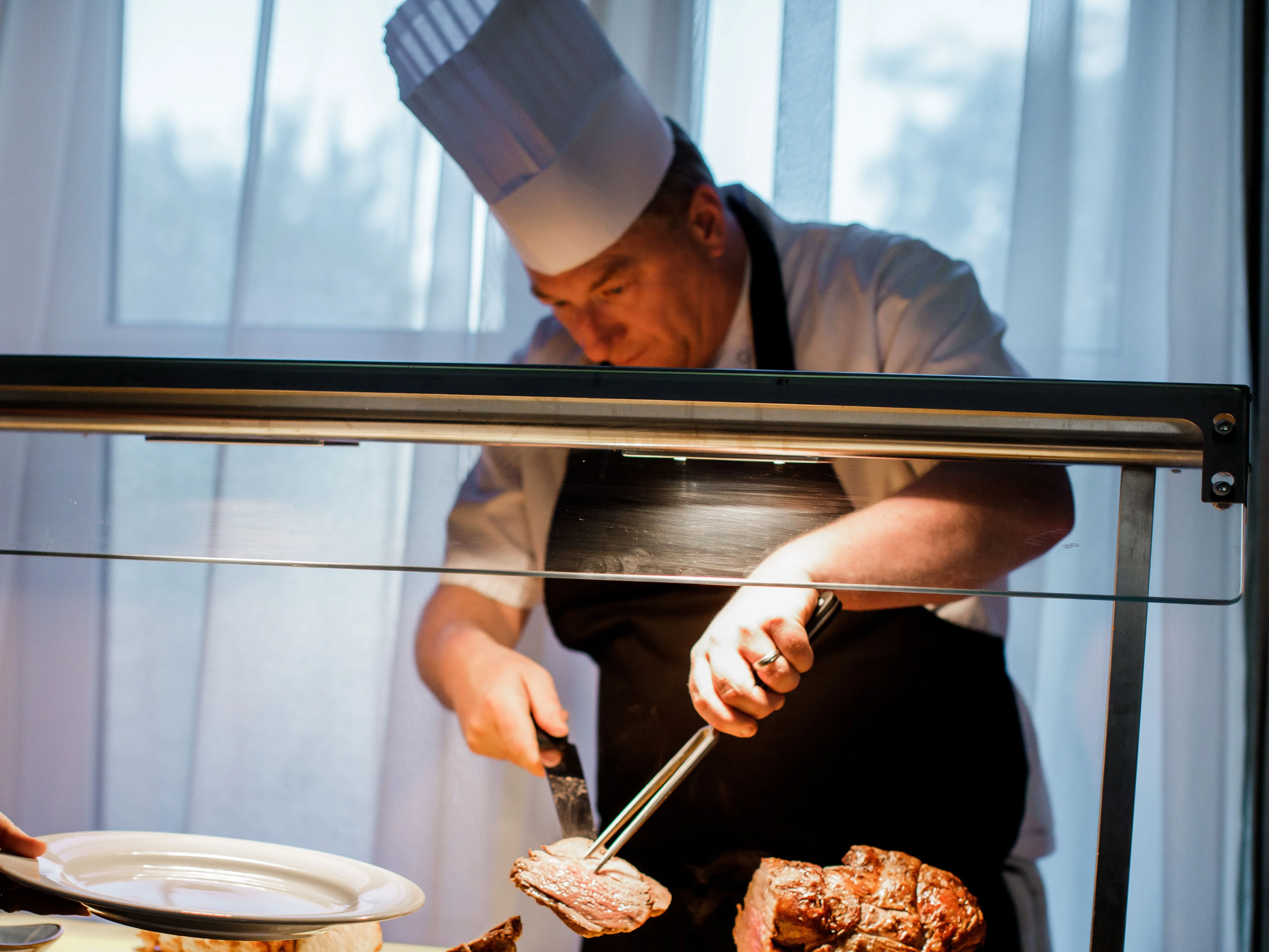 Chef carving roast meat at a serving station while a guest holds out a plate