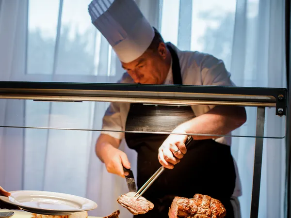 Chef carving roast meat at a serving station while a guest holds out a plate