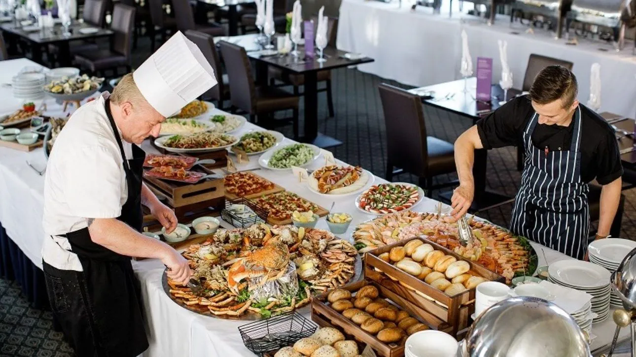 Two chefs arranging an extensive buffet with seafood, breads and salads in a restaurant dining room.
