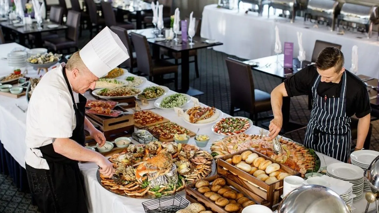 Two chefs arranging an extensive buffet with seafood, breads and salads in a restaurant dining room.