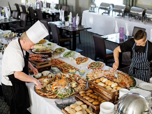 Two chefs arranging an extensive buffet with seafood, breads and salads in a restaurant dining room.