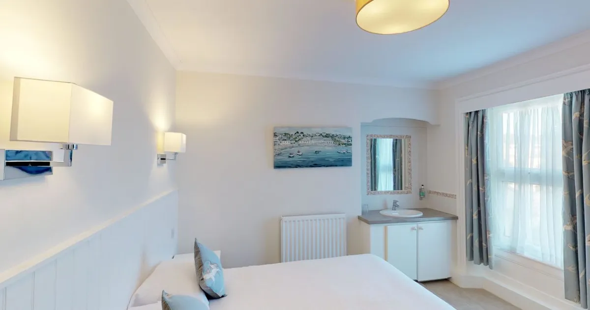 Bright, modern bedroom with a double bed, soft lighting, large bay window and in-room washbasin.