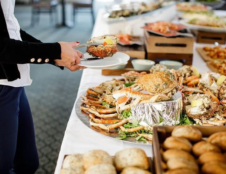 Person serving seafood from a buffet platter with crab and shellfish