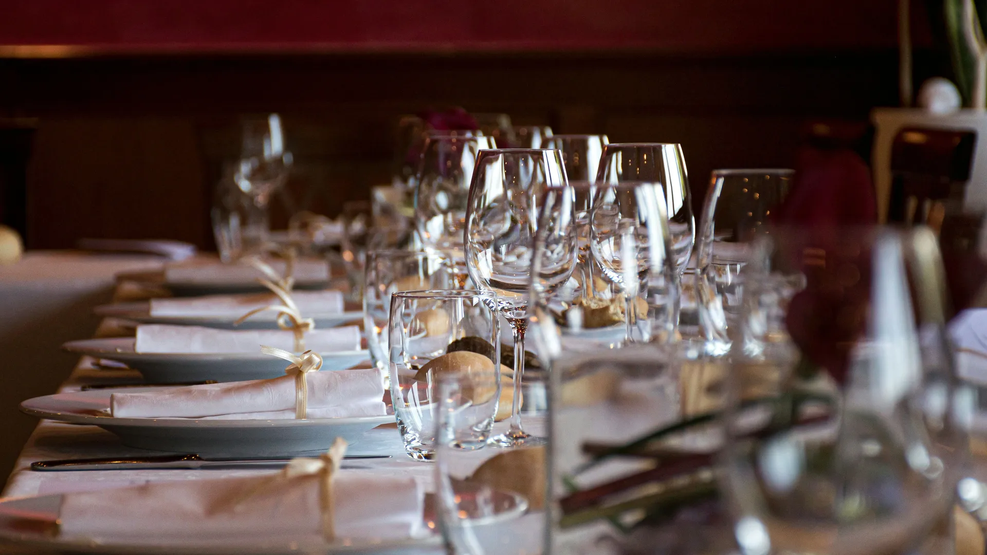 Elegantly set restaurant table with white plates, folded napkins and rows of wine glasses