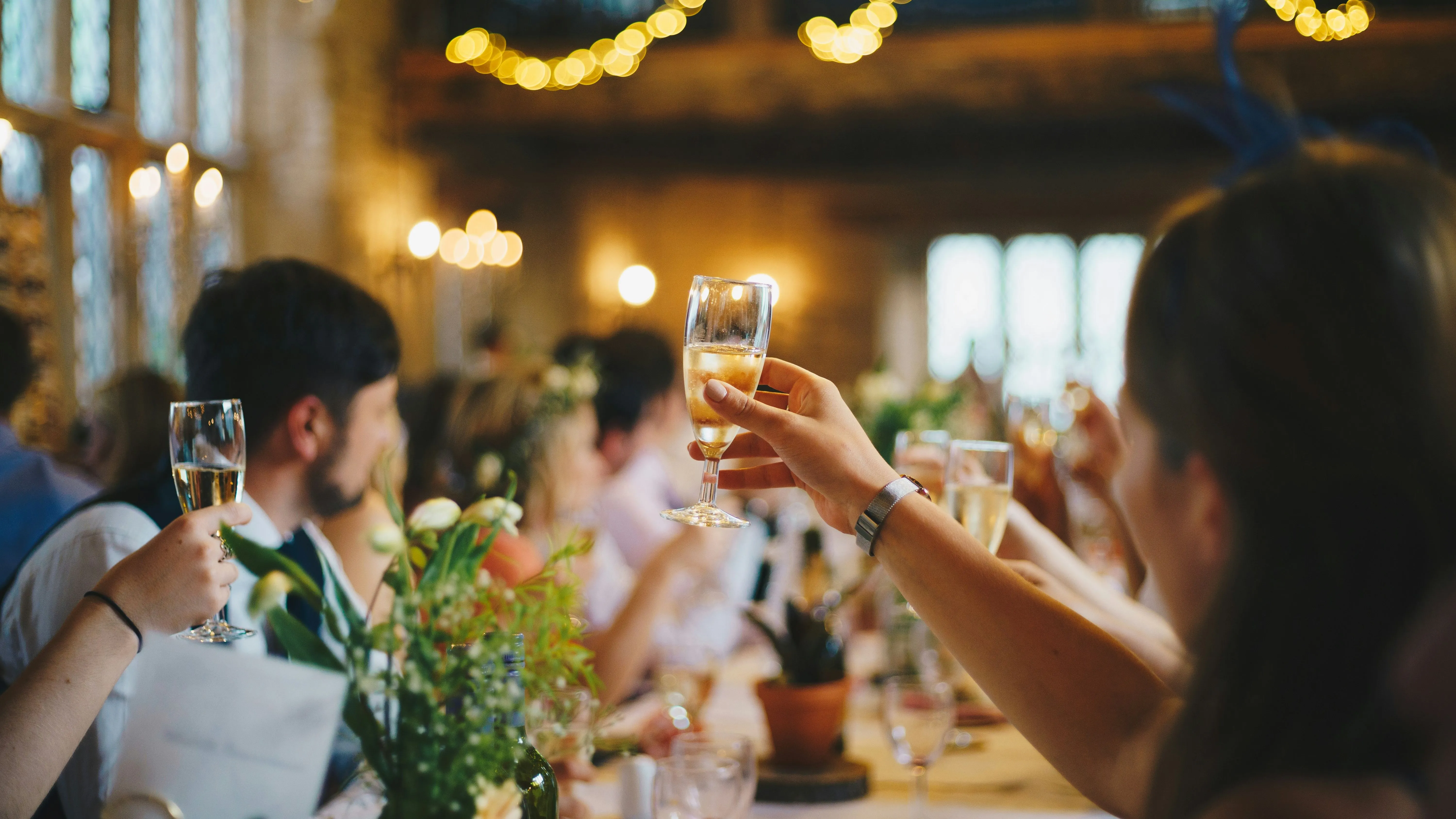Guests raising glasses of champagne during a celebration in a warmly lit rustic venue