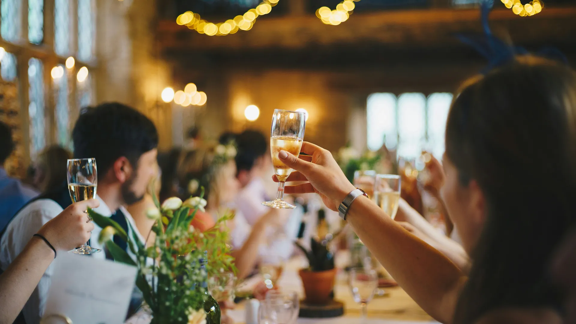 Guests raising glasses of champagne during a celebration in a warmly lit rustic venue