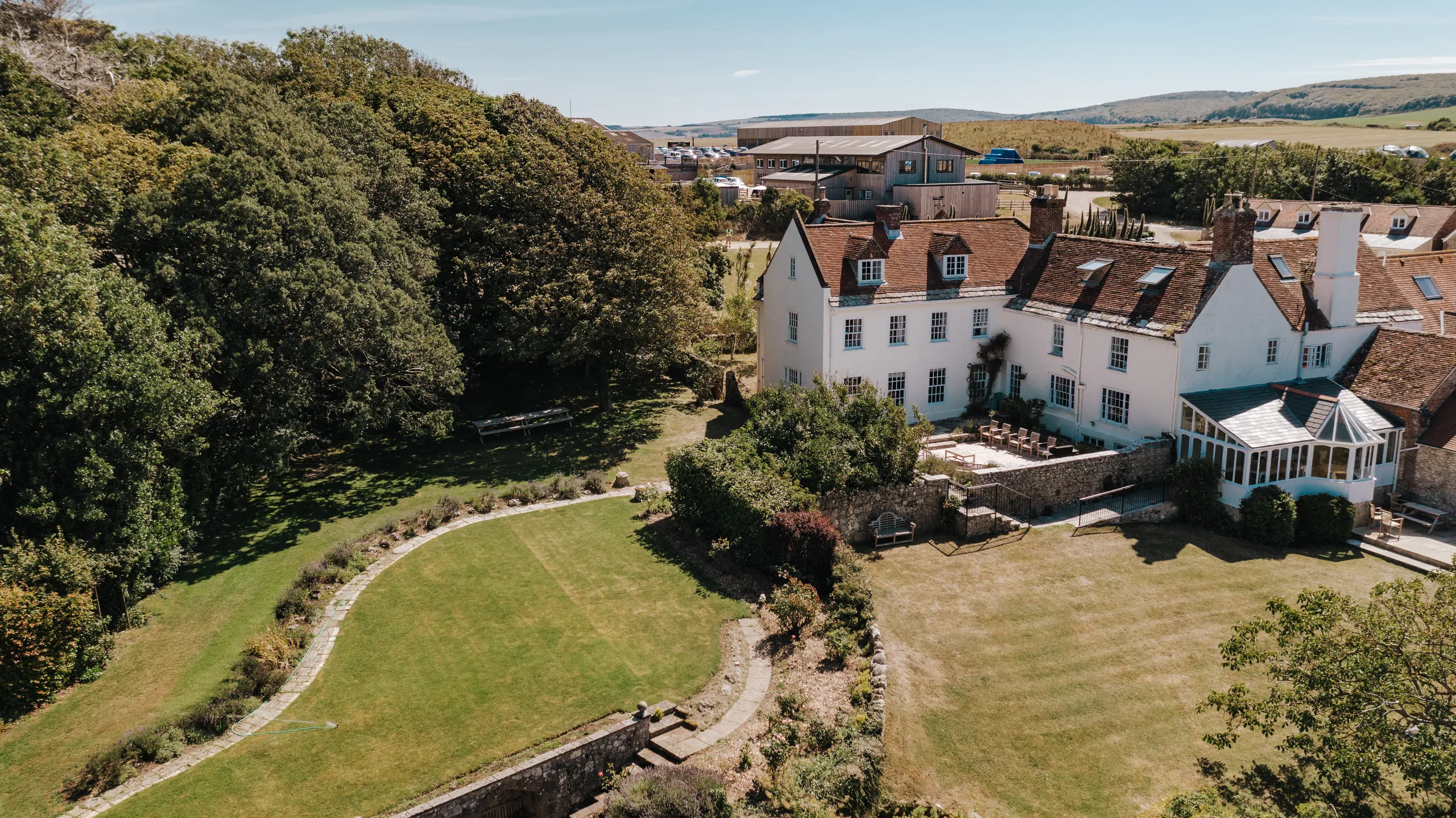 Aerial view of Tapnell Manor with white country house, terraced patio and large gardens bordered by woodland