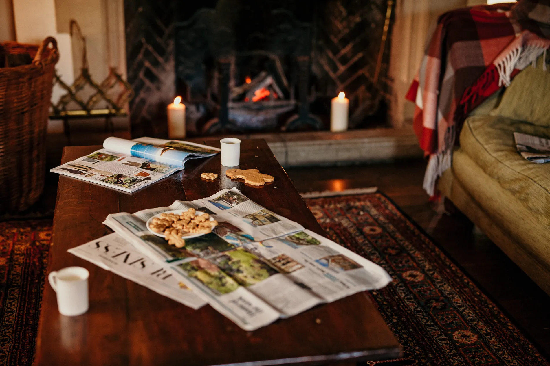 Cosy living room with a lit fireplace, candles and a wooden coffee table with magazines, biscuits and mugs