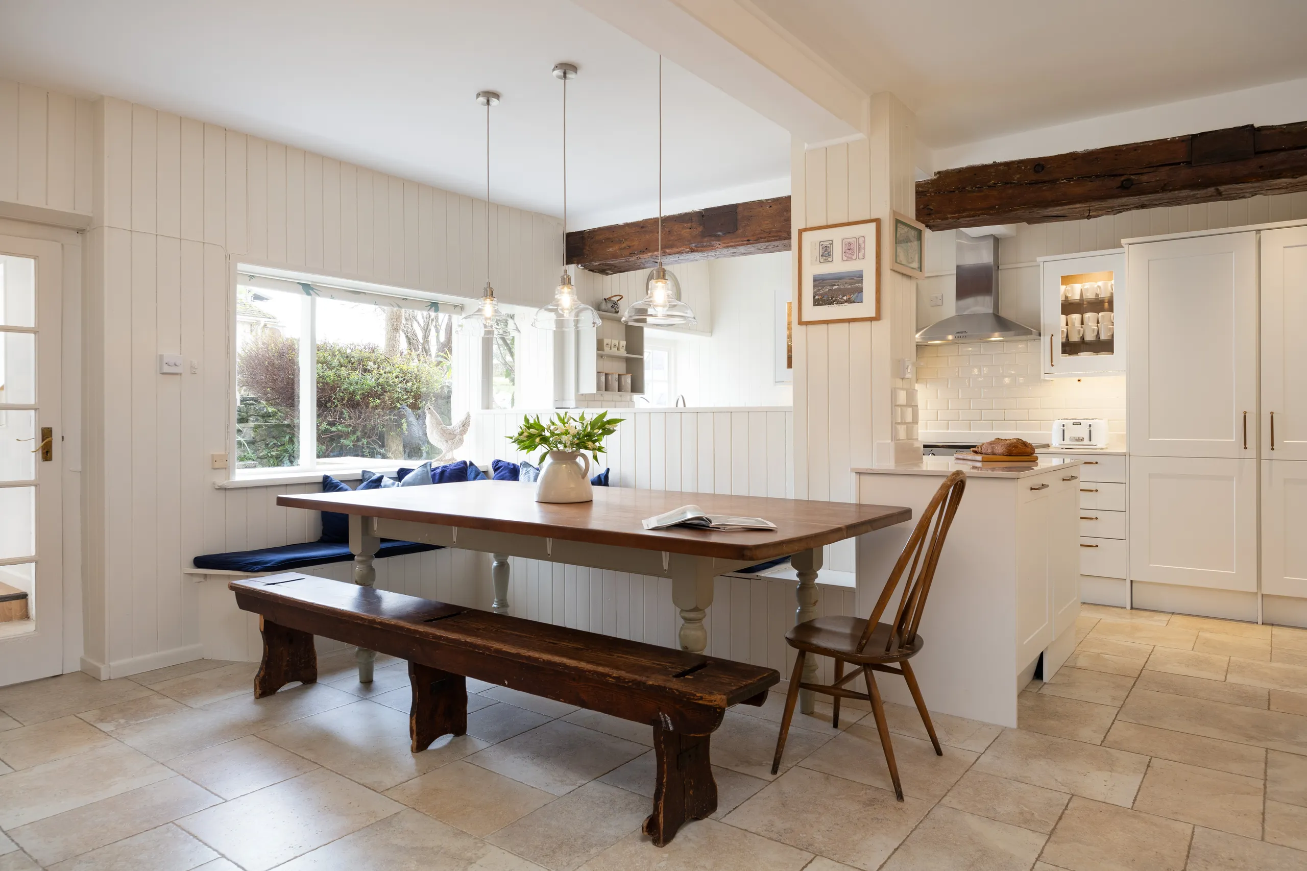 Light, modern farmhouse kitchen with wooden dining table, bench seating and white cabinetry