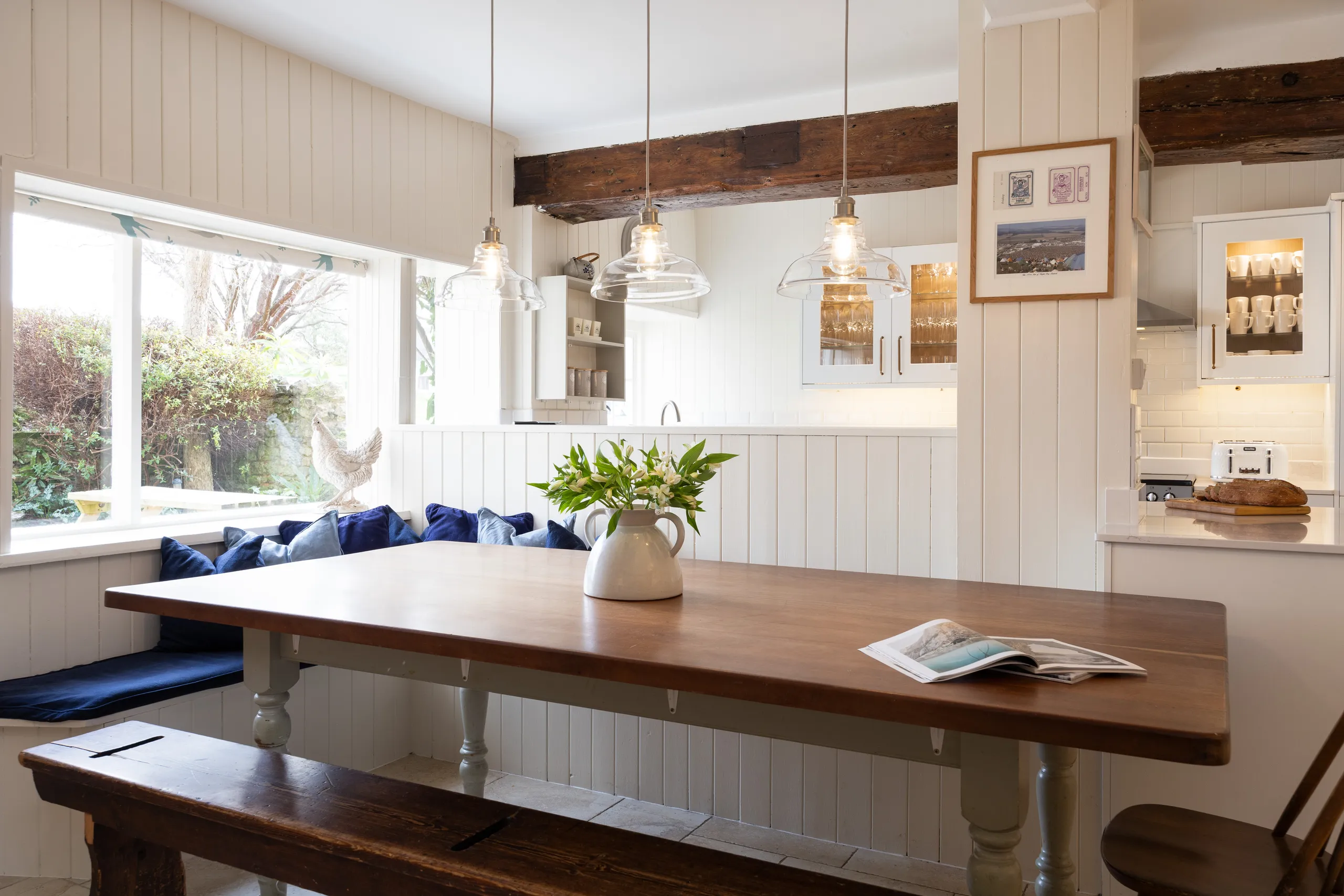Cosy farmhouse kitchen dining area with wooden table, window seat and glass pendant lights