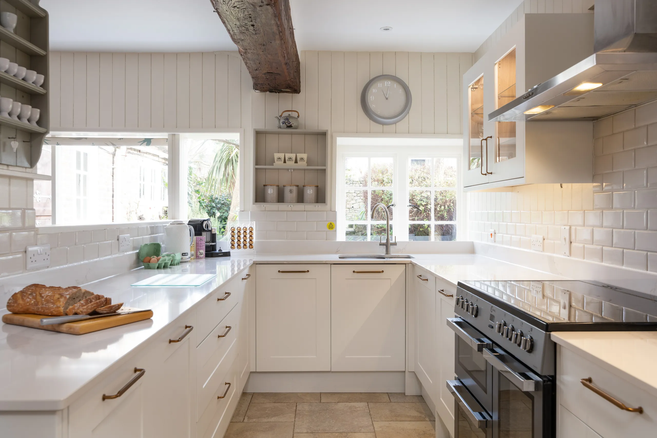 Bright country-style kitchen with white cabinets, subway tiles, range cooker and a wooden ceiling beam